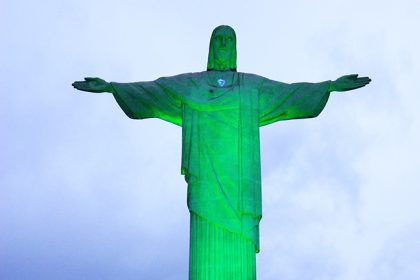 Le Christ Rédempteur de Rio illuminé en vert, symbolisant la transition énergétique et la coopération France-Brésil autour de l'hydrogène vert, accompagnée de doutes sur un éventuel agenda économique dissimulé.