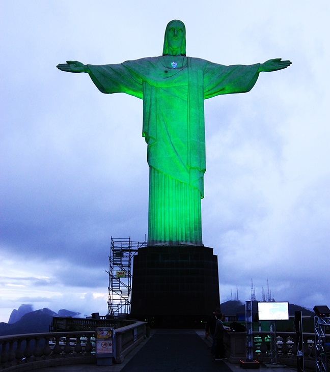 Le Christ Rédempteur de Rio illuminé en vert, symbolisant la transition énergétique et la coopération France-Brésil autour de l'hydrogène vert, accompagnée de doutes sur un éventuel agenda économique dissimulé.